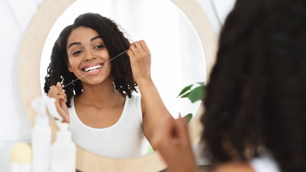 Woman looking in the mirror while flossing her teeth